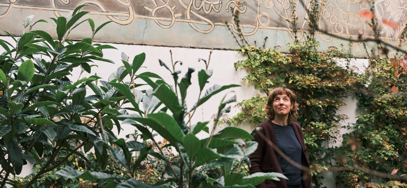 Ellen Desmet voor hoge witte muur met planten op de voorgrond.