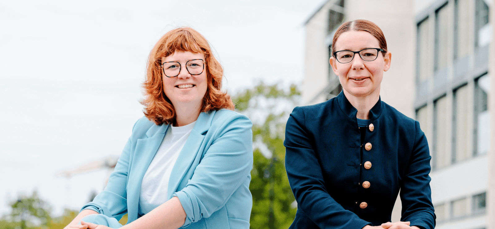 Twee jonge vrouwen in formele, blauwe kledij kijken voor zich uit.