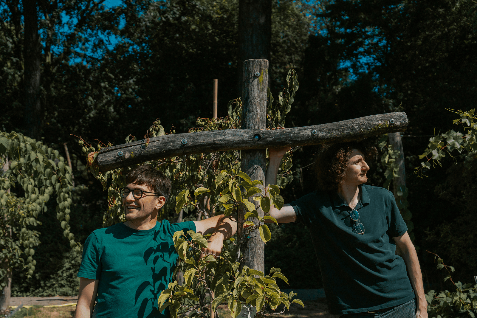 Twee jonge mannen leunen tegen een houten kruis in een tuin - leonardo en victor.