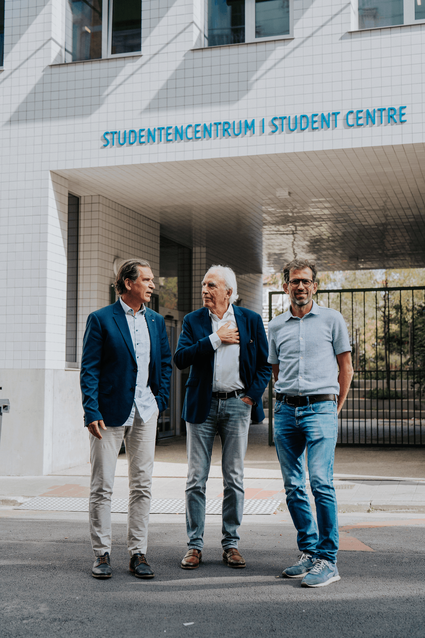 Drie formeel geklede mannen voeren een gesprek voor het studentencentrum