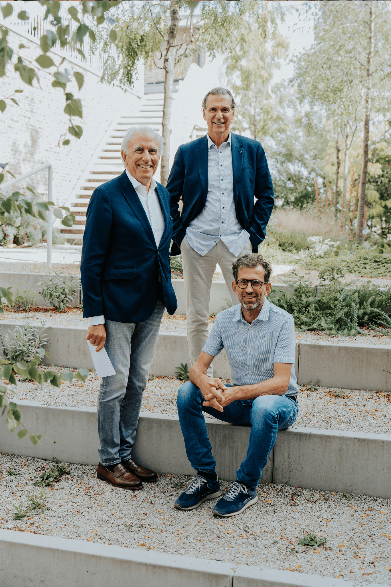 Drie formeel geklede mannen poseren in een trappentuin.