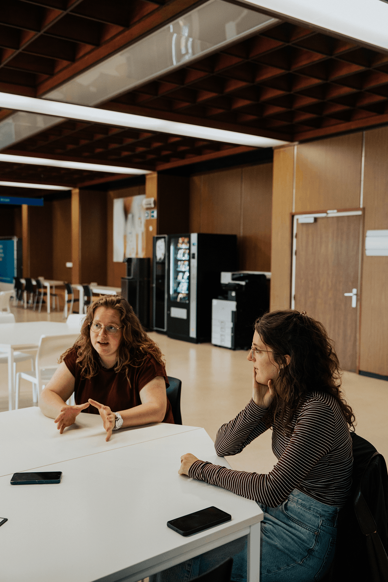 Twee jonge vrouwen, Charlotte en Rune vertellen een verhaal aan een witte tafel.