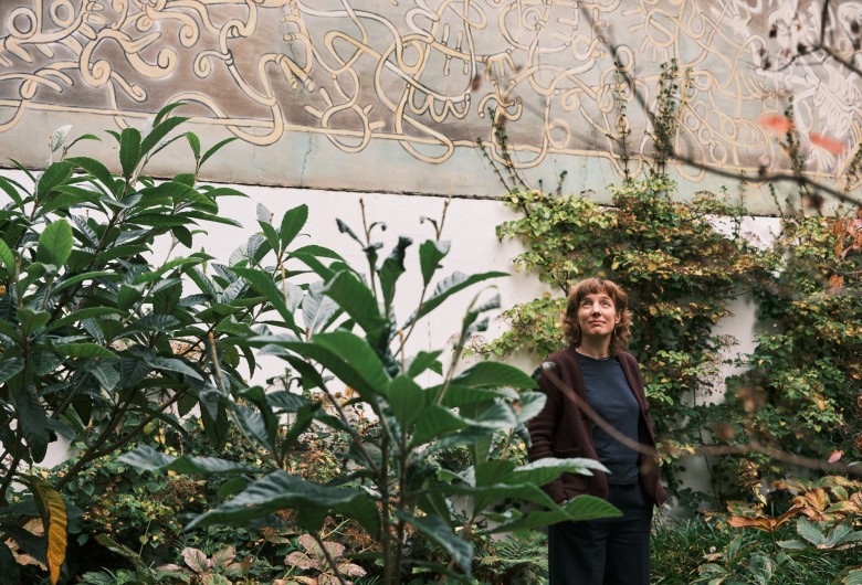 Ellen Desmet voor hoge witte muur met planten op de voorgrond.