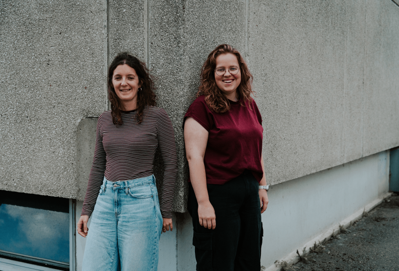 Twee jonge vrouwen leunen tegen de hoek van een home van UGent.