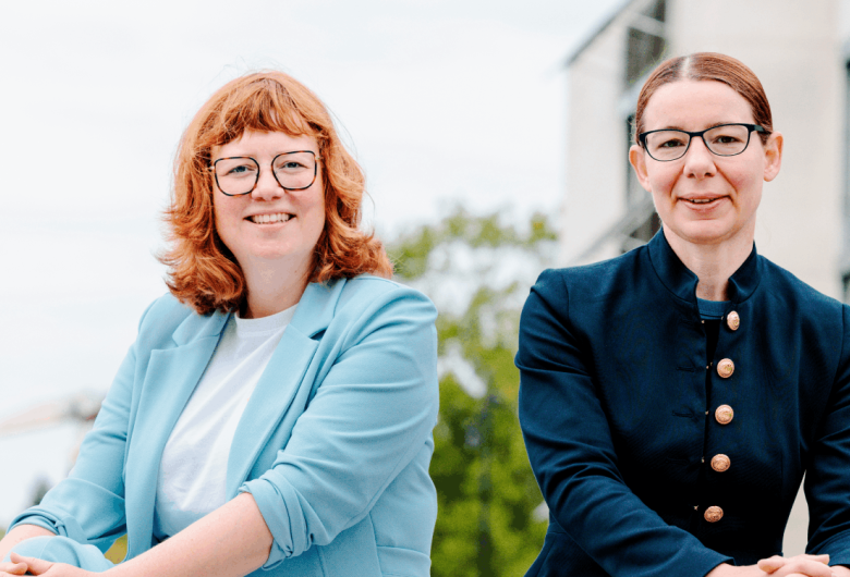 Twee jonge vrouwen in formele, blauwe kledij kijken voor zich uit.