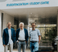 Drie formeel geklede mannen poseren voor het studentencentrum van UGent.