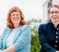 Twee jonge vrouwen in formele, blauwe kledij kijken voor zich uit.